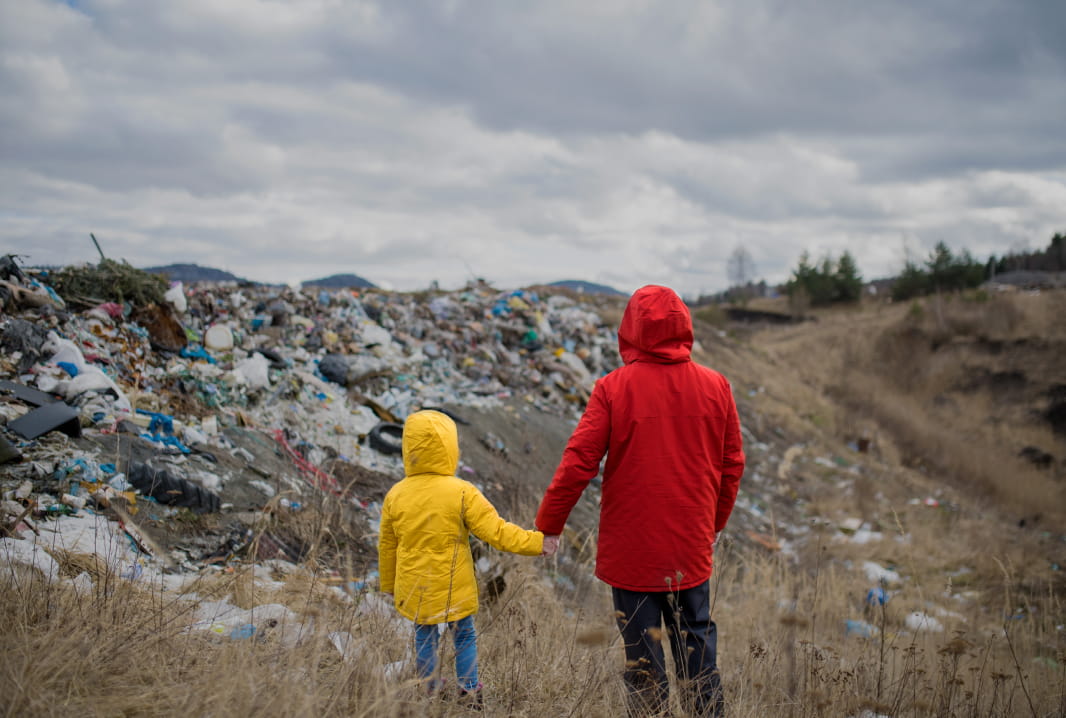 Rear view of man and child in raincoats standing in a landfill